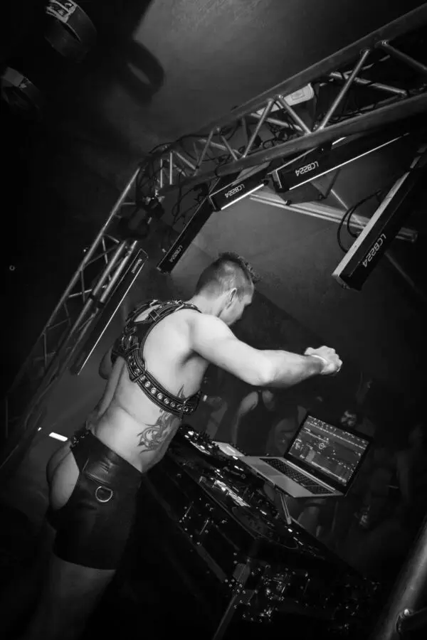 Bearded man in a leather harness holding a flogger